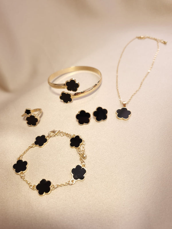 The Set trifoi Negru - auriu 5 piese by Lucky Charm features gold jewelry with black flower-shaped charms, including a ring, bracelet, bangle, necklace, and earrings, elegantly displayed on soft beige cloth.