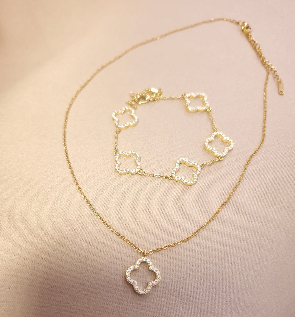 Gold clover pendant necklace and bracelet with sparkling stones from Lucky Charms Trifoi Auriu Set, displayed on a light beige surface.
