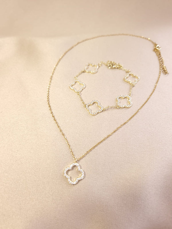 The Set Trifoi Auriu cu pietre stralucitoare by Lucky Charm, featuring a delicate gold necklace and matching bracelet with interlocking clover pendants adorned with small pearls, is elegantly displayed on soft beige fabric.